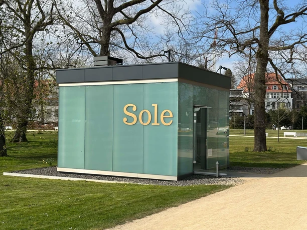 Gläserner Sole-Pavillon im Kurpark Bad Salzuflen zwischen Bäumen und Rasenflächen