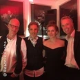Vier Personen lächeln in die Kamera, sie tragen elegante Kleidung bei einem stimmungsvoll beleuchteten Event.