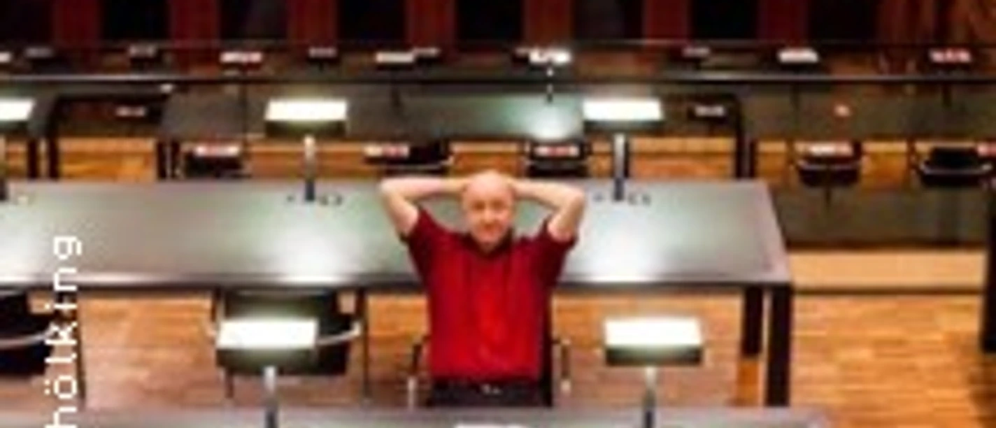 Eine Person sitzt entspannt an einem großen Tisch in einer modernen, gut beleuchteten Bibliothek.