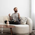 Ein Mann mit Bart sitzt entspannt auf einem hellen Sofa, umgeben von einem minimalistischen Raum.