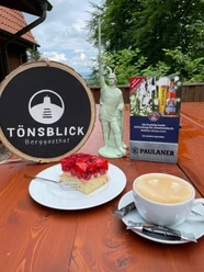 Berggasthof Tönsblick Vorne ein Stück Erdbeerkuchen und Kaffee auf einem Tisch, hinten ein Schild "Tönsblick".