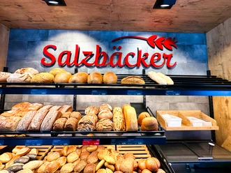 Eine Auswahl des Sortiments Regale voller frischer Brote und Brötchen unter dem roten Logo Salzbäcker.