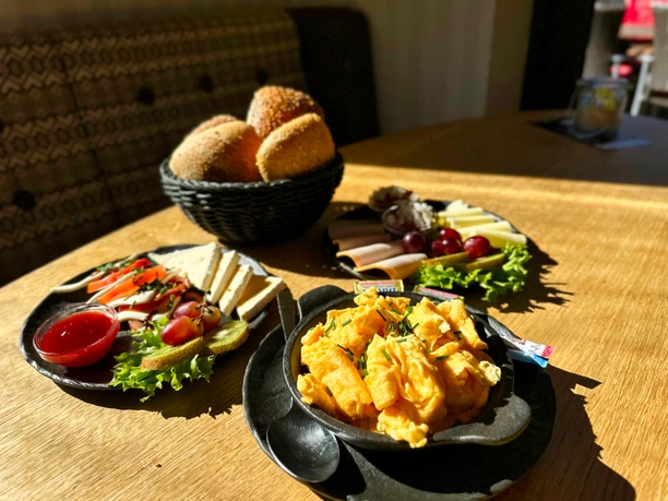 Ein Genießer-Frühstück mit Rührei, Käse, Wurst, Obst und einem Korb mit frischen Brötchen.