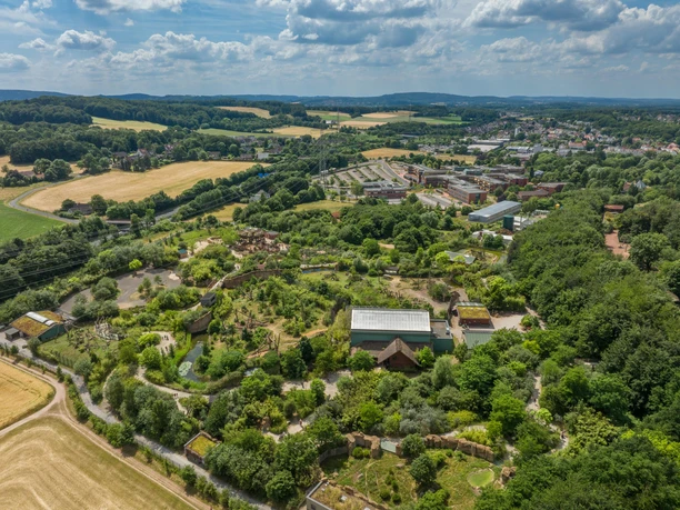 Luftaufnahme des Osnabrücker Zoos Luftaufnahme einer weitläufigen, grünen Landschaft mit Gebäuden und Feldern im Hintergrund.