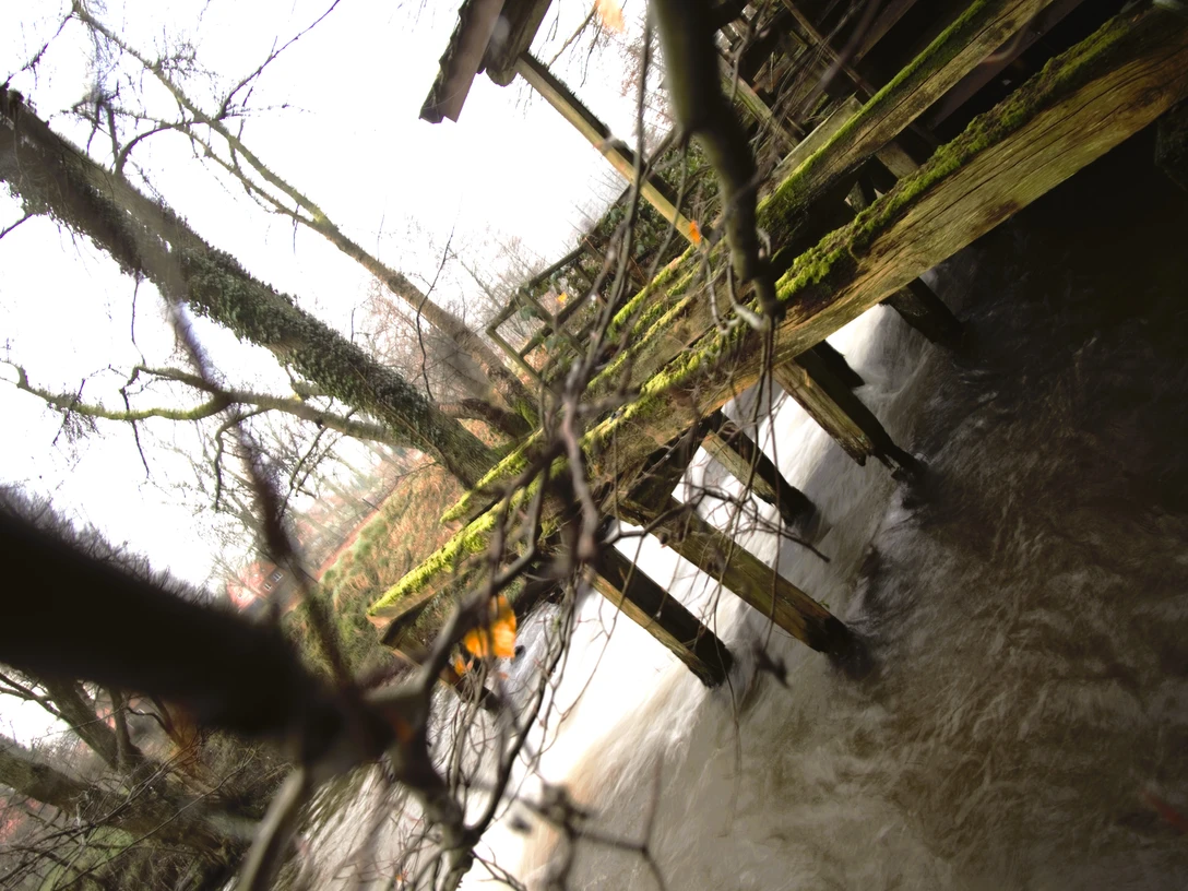 Soderstorf Mühle .jpg Ein moosbewachsener Steg führt über einen fließenden Bach, umgeben von kahlen Ästen und winterlicher Natur.