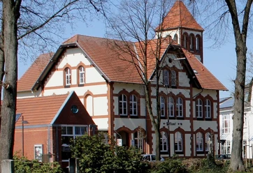 postamt__1__.jpg Historisches Gebäude mit rotem Satteldach und Turm, umgeben von Bäumen, bei sonnigem Wetter.