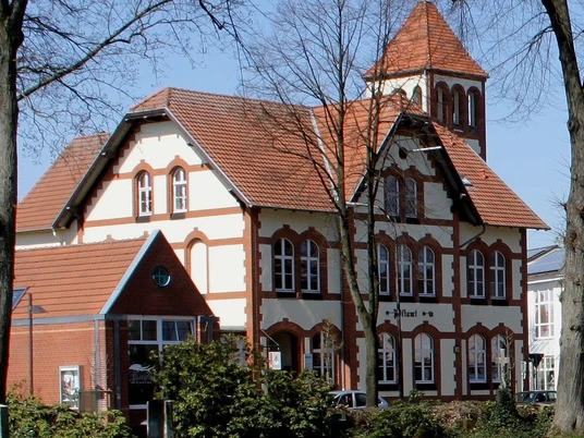 postamt__1__.jpg Historisches Gebäude mit rotem Satteldach und Turm, umgeben von Bäumen, bei sonnigem Wetter.