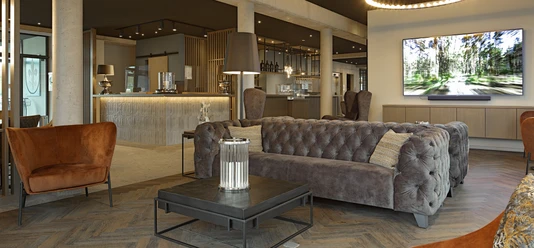Hotel-Zeitgeist_Warburg_neu.JPG Moderner Hotel-Lounge-Bereich mit grauen gepolsterten Sofas, rustikalen Holzmöbeln und gedämpfter Beleuchtung.