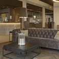 Hotel-Zeitgeist_Warburg_neu.JPG Moderner Hotel-Lounge-Bereich mit grauen gepolsterten Sofas, rustikalen Holzmöbeln und gedämpfter Beleuchtung.
