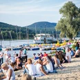 Strandbesucher am Schiedersee entspannen, während Segelboote und ein Ausflugsdampfer vorbeiziehen.
