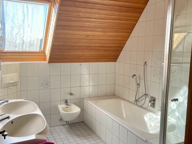 Fewo_Liemke_Bad_SHSCC-BY-SA_Teutoburger_Wald_Stadt_Schloss_Holte-Stukenbrock Modernes Badezimmer mit Dachfenster, Doppelwaschbecken, Badewanne, Bidet und schräger Holzdecke.