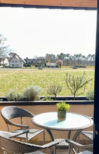 Ein Balkon mit Tisch und vier Stühlen bietet Blick auf ein weites Feld unter einem bewölkten Himmel.
