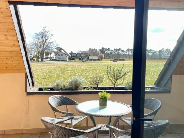 Ein Balkon mit Tisch und vier Stühlen bietet Blick auf ein weites Feld unter einem bewölkten Himmel.