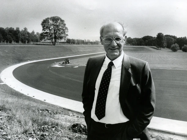 Nixdorf am Ahorn Sportpark Eine ältere Person im Anzug steht vor einem leeren Sportplatz mit einer umlaufenden Laufbahn.