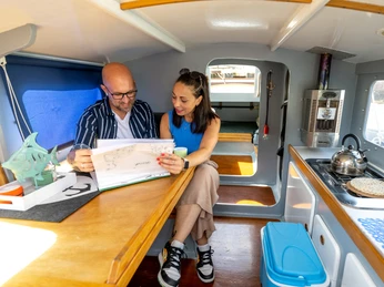 Escargot-Tour, Mülheim an der Ruhr Mann und Frau sitzen am Tisch im Innenraum eines Hausboots (Escargot) und blättern durch Infomaterial