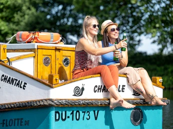 Escargot-Tour, Mülheim an der Ruhr Zwei Frauen sitzen sonnenbeschienen auf einem Hausboot mit Getränken in der Hand.