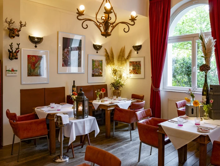 Grubers Restaurant Gemütlich eingerichtetes Restaurant mit roten Lederstühlen und verschnörkelndem Kronleuchter.Comfortably furnished restaurant with red leather chairs and an ornate chandelier.