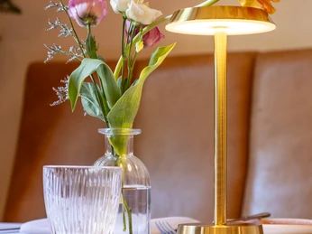 Grubers Restaurant Nahaufnahme, gedeckter Tisch, Vase mit dezenten Blumen und goldener Tischleuchte.Close-up of a table setting: vase with modest flowers and golden table lamp.
