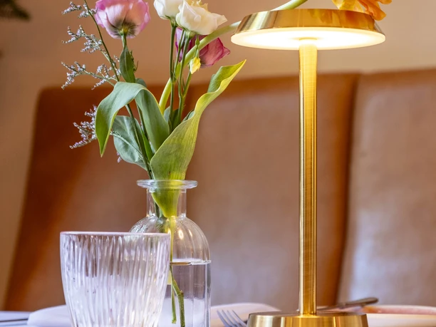 Grubers Restaurant Close-up of a table setting: vase with modest flowers and golden table lamp.