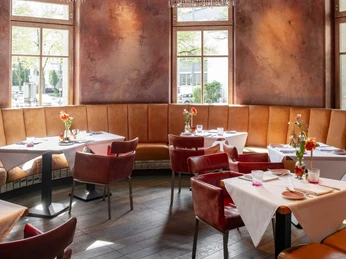 Grubers Restaurant Edle Inneneinrichtung mit Ledergarnitur und terrakottafarbigen Wände. Von der lila Decke hängt ein imposanter Kronleuchter aus Glasperlenketten. Noble interior design with leather furniture and terracotta-colored walls. An imposing chandelier made of glass beads hangs from the purple ceiling.