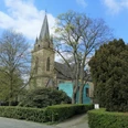 Eine historische Kirche in Herford, umgeben von hohen Bäumen und einer gepflegten Grünanlage.