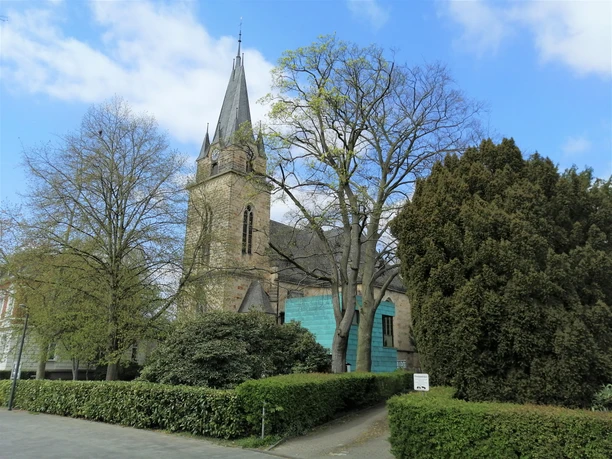 Eine historische Kirche in Herford, umgeben von hohen Bäumen und einer gepflegten Grünanlage.