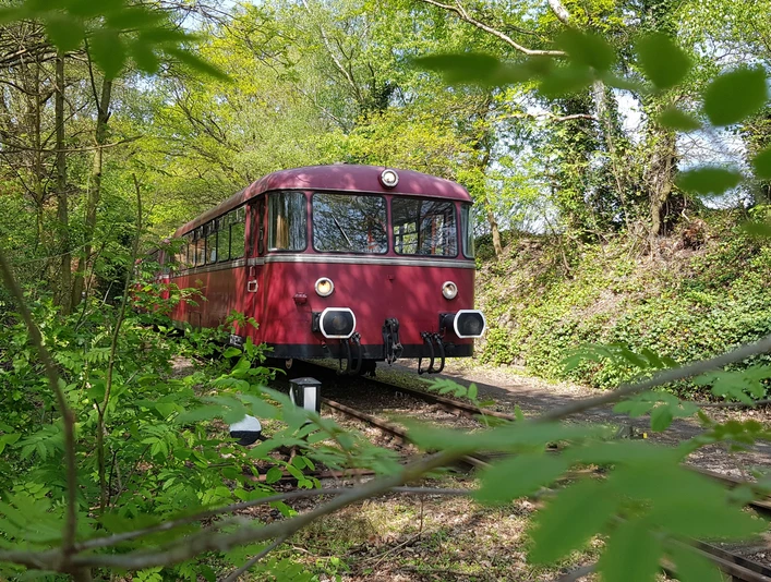 Museumsbahn MRU Roter Triebwagen fährt durch grünen, bewaldeten Abschnitt einer Museumsbahnstrecke im Frühling.