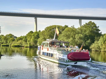 Weiße Flotte im Ruhrtal, Mülheim an der Ruhr Ein Ausflugsboot mit Passagieren fährt auf einem Fluss, im Hintergrund eine Brücke und Bäume.