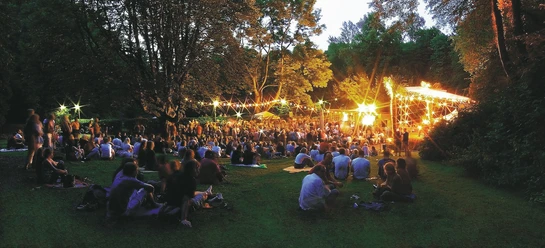 Die Freilichtbühne in der Mülheimer Altstadt Freilichtbühne in Mülheim an der Ruhr bei Abenddämmerung, mit Publikum in dichter Baumkulisse.