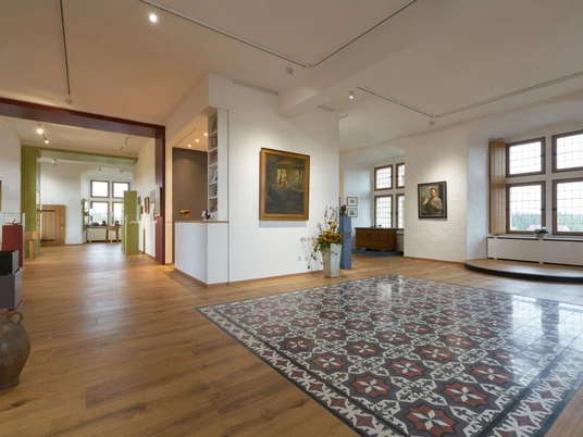 Ein helles Museum mit großen Fenstern, modernen Elementen und traditionellen Kunstwerken in einem großzügigen Raum.