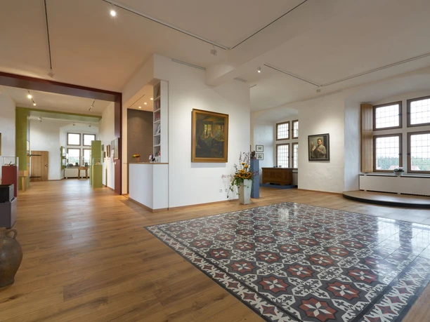 Ein helles Museum mit großen Fenstern, modernen Elementen und traditionellen Kunstwerken in einem großzügigen Raum.