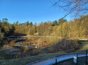 Wingst_Spielpark_Sommerrodelbahn Sommerrodelbahn schlängelt sich durch bewaldete Hänge des Spielparks Wingst unter blauem Himmel.Summer toboggan run winds its way through the wooded slopes of the Wingst play park under a blue sky.Sommerkælkebakken snor sig gennem de skovklædte skråninger i Wingst Legepark under en blå himmel.De zomerrodelbaan baant zich onder een blauwe hemel een weg door de beboste hellingen van het speelpark Wingst.