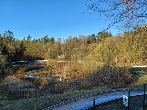 Wingst_Spielpark_Sommerrodelbahn Sommerrodelbahn schlängelt sich durch bewaldete Hänge des Spielparks Wingst unter blauem Himmel.