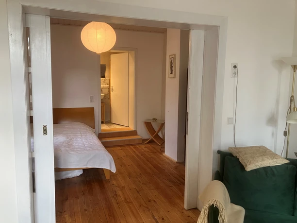 Fewo Beim Johannistor.jpg Ein gemütliches Apartment mit Holzdielen, Schlafzimmer, Sofa und Blick in eine helle Küche.