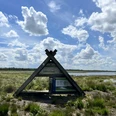 Blick ins Provinzialmoor, Naturschutzgebiet in Twist ©Emsland Tourismus GmbH (1).JPEG Dreieckige Infotafel aus Holz im Moorgebiet mit Wasserflächen, Wolkenhimmel und weiter Landschaft.