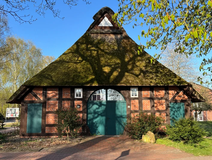 Haus auf der Wurth Fachwerkhaus mit Reetdach und grüner Tür, umgeben von Bäumen, in frühlingshafter Landschaft.