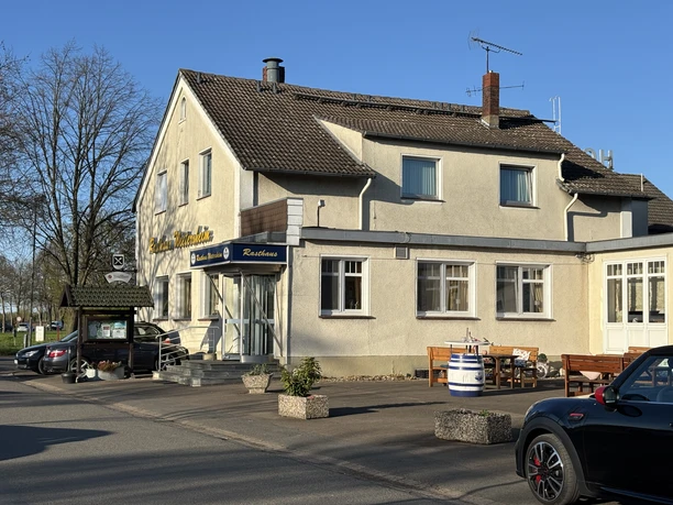 Zweistöckiges Gasthaus mit gelber Fassade, Sitzbänken vor dem Eingang, umgeben von Bäumen.