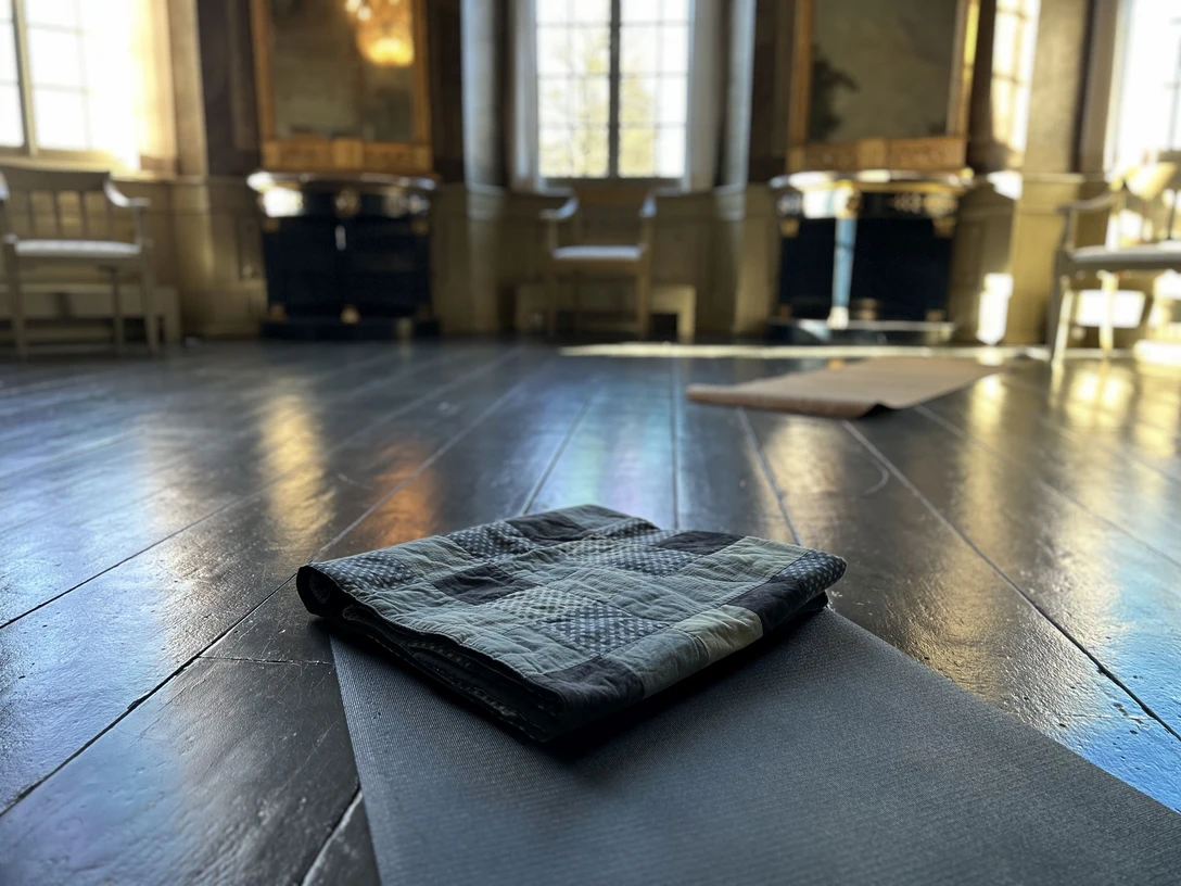 Yoga im Gartensaal Yoga-Matte auf dunklem Holzboden in einem lichtdurchfluteten historischen Saal mit großen Fenstern.