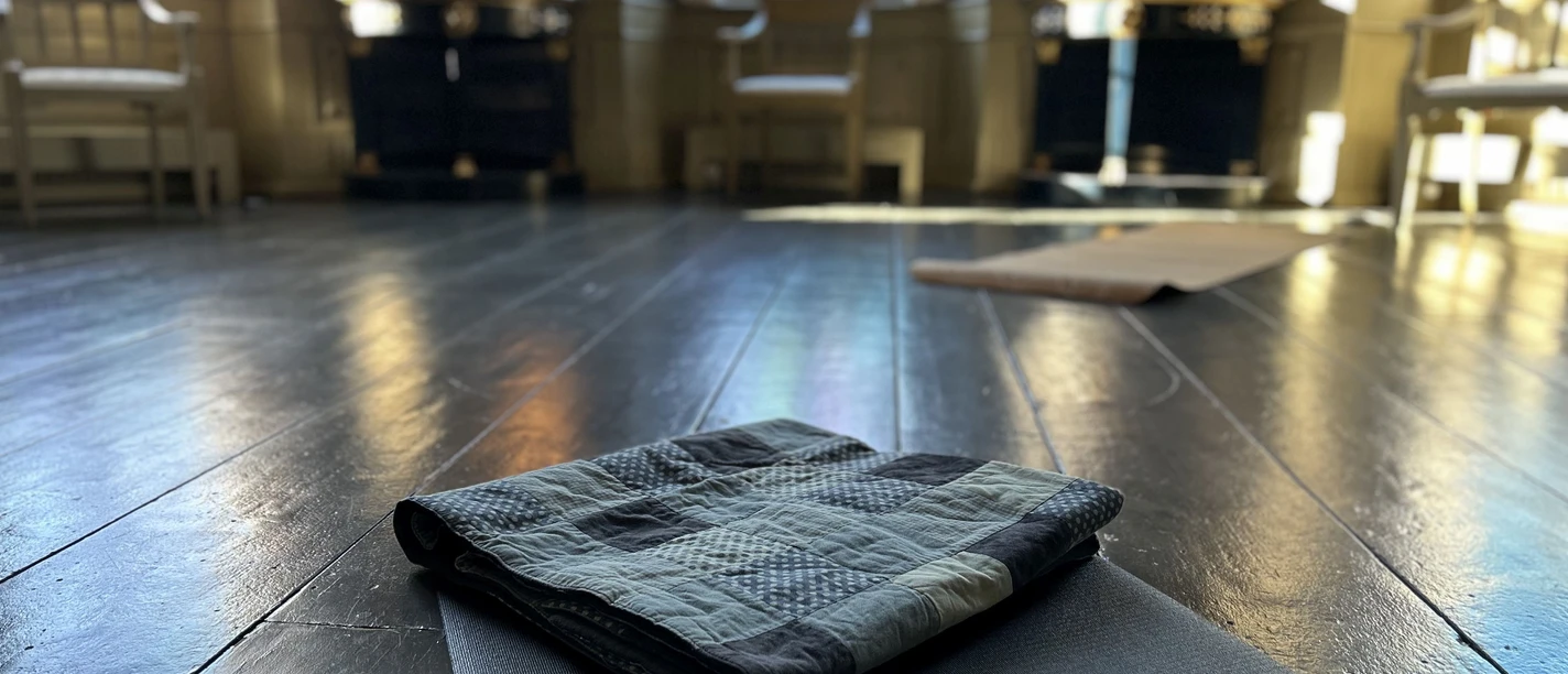 Yoga im Gartensaal Yoga-Matte auf dunklem Holzboden in einem lichtdurchfluteten historischen Saal mit großen Fenstern.