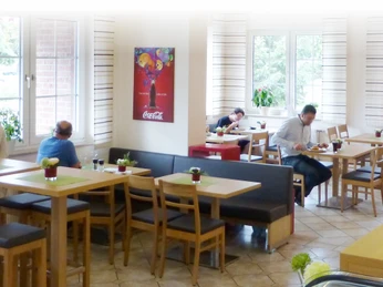 Mehrere Gäste sitzen an Holztischen in einem lichtdurchfluteten Restaurant mit gemütlicher Atmosphäre.