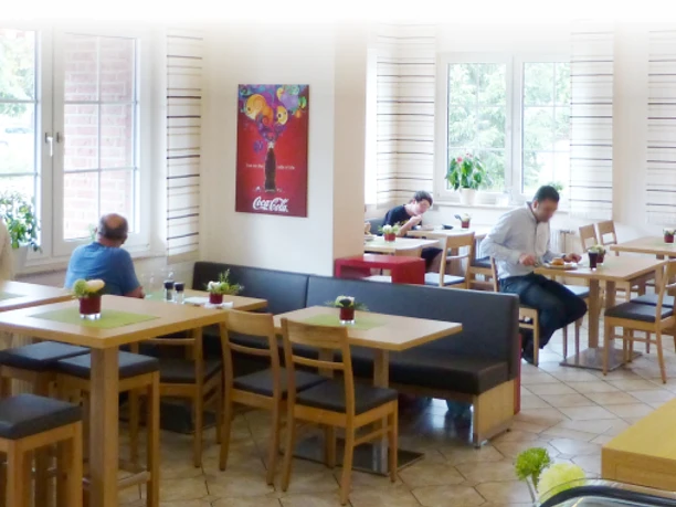 Mehrere Gäste sitzen an Holztischen in einem lichtdurchfluteten Restaurant mit gemütlicher Atmosphäre.