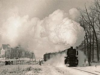 digitales_museum_haller_zeitraeume_haller_willem_dampflok.1963_joerg_buck._lupe_1.jpg Eine Dampflokomotive zieht einen Zug durch eine verschneite Landschaft, riesige Dampfwolken aufsteigend.