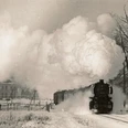 digitales_museum_haller_zeitraeume_haller_willem_dampflok.1963_joerg_buck._lupe_1.jpg Eine Dampflokomotive zieht einen Zug durch eine verschneite Landschaft, riesige Dampfwolken aufsteigend.