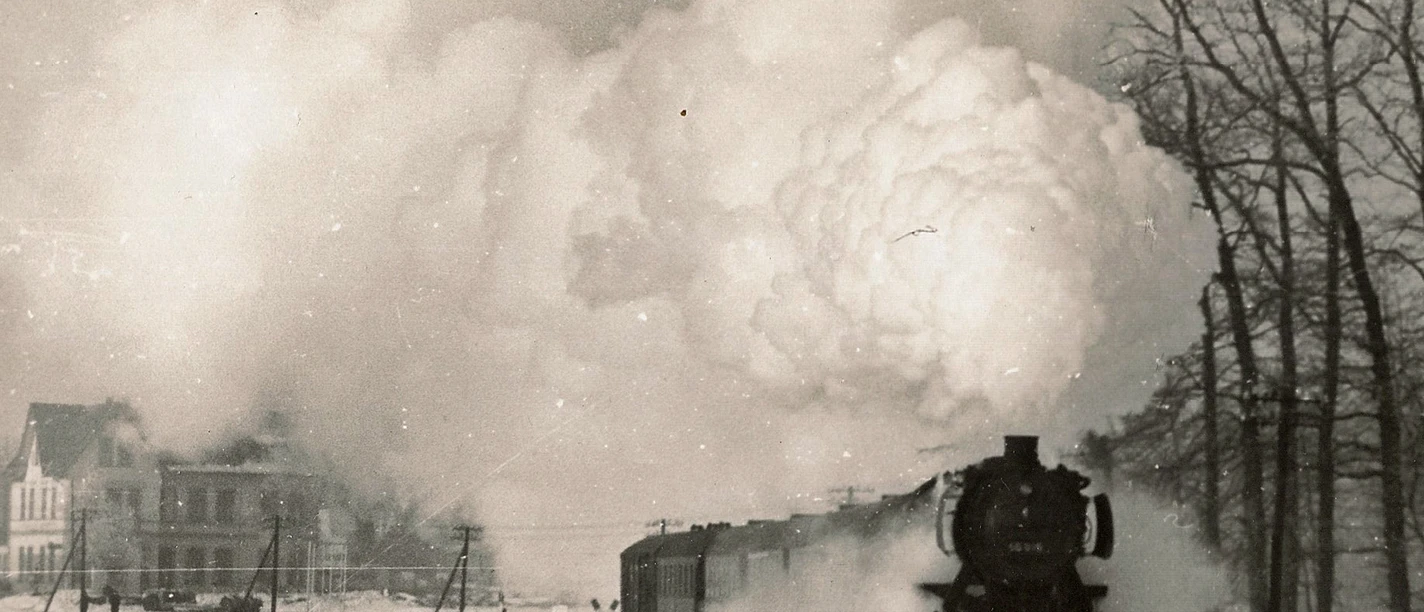 digitales_museum_haller_zeitraeume_haller_willem_dampflok.1963_joerg_buck._lupe_1.jpg Eine Dampflokomotive zieht einen Zug durch eine verschneite Landschaft, riesige Dampfwolken aufsteigend.