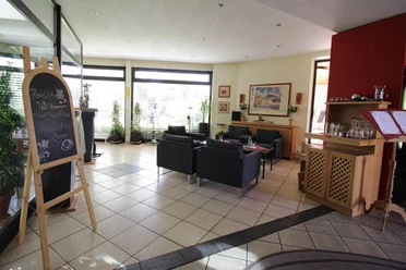 Eingangsbereich Hotel Lindenkrug Heller Eingangsbereich mit Sitzgruppen, Theke, Pflanzen und Informationstafel nahe der Glastür