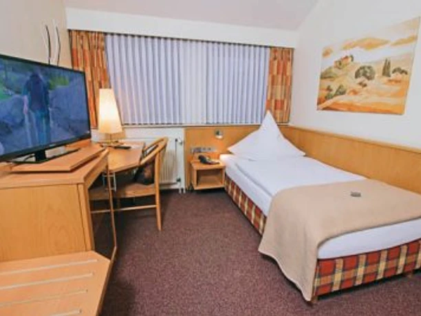 Einzelzimmer mit Einzelbett, Schreibtisch, Fernseher, Fenster mit Lamellen und Wandbild