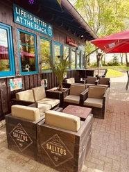 Beachbar 12 am Badesee Lahde Außenbereich einer Strandbar mit Holzmöbeln, Schildern und Sonnenschirmen nahe eines Badesees.