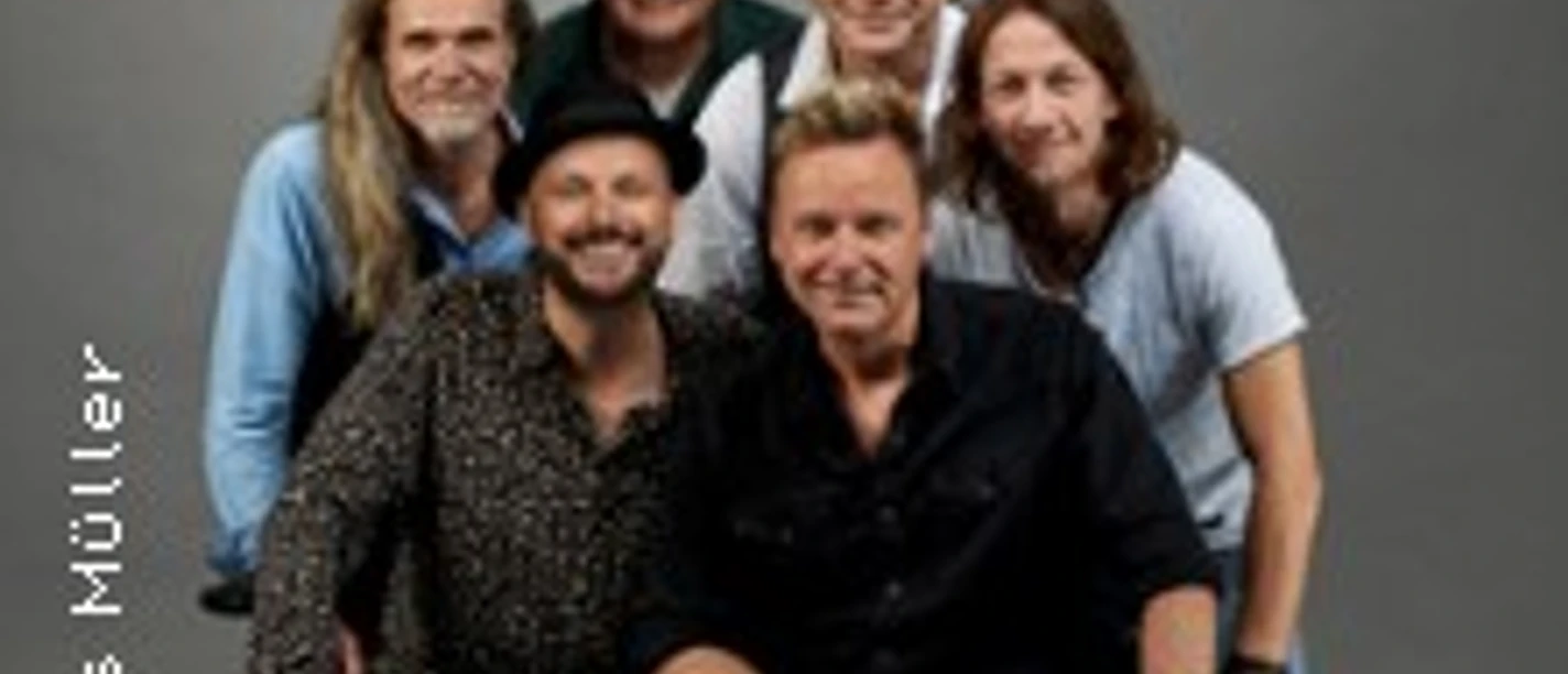 Sechs Musiker posieren lächelnd vor grauem Hintergrund. Vier sitzen, zwei stehen dahinter.