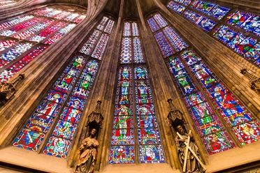 Aachener Dom Blick nach oben entlang der bunten Fenster des Aachener Doms, zwischen denen Säulen mit Statuen stehen.