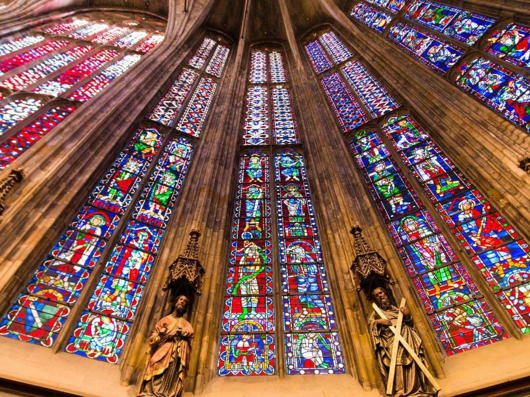 Aachener Dom Blick nach oben entlang der bunten Fenster des Aachener Doms, zwischen denen Säulen mit Statuen stehen.